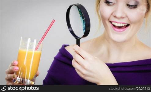 Blonde woman holding magnifying glass investigating and looking closely at glass with orange juice.. Woman holding magnifying glass investigating juice
