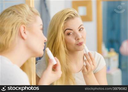Blonde woman in bathroom putting applying lip balm moisturizing balsam, taking care of her lips skin.. Woman in bathroom applying lip balm