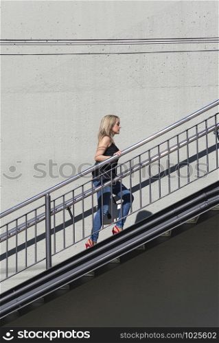Blonde woman in casual wear walking up stairs outdoor in the city