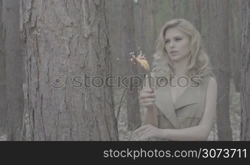 blonde woman in the forest holding a fire fountain