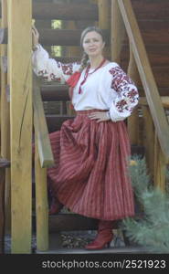 Blonde woman in traditional ukrainian clothing with embroidery posing on wooden stairs. Concept of cultural diversity, outdoor lifestyle.