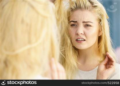 Blonde woman looking at her dry split ended hair. Female having haircare problems being sad about it.. Woman having problem with her hair
