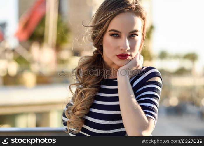 Blonde woman, model of fashion, standing in urban background. Beautiful young girl wearing striped t-shirt and blue jeans in the street. Pretty russian female with pigtai and blue eyes.