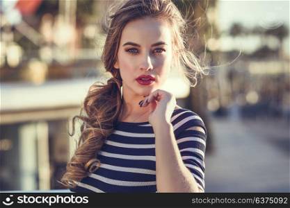 Blonde woman, model of fashion, standing in urban background. Beautiful young girl wearing striped t-shirt and blue jeans in the street. Pretty russian female with pigtai and blue eyes.