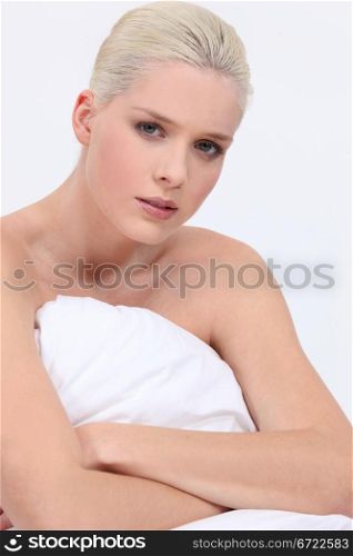 blonde woman naked sitting on bed with a neutral face expression