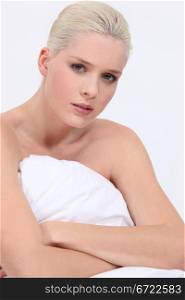 blonde woman naked sitting on bed with a neutral face expression