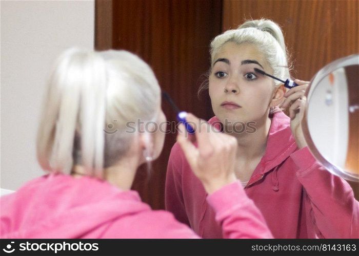 Blonde woman painting her eyebrows in front of the mirror