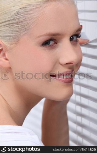 Blonde woman peeking through venetian blinds