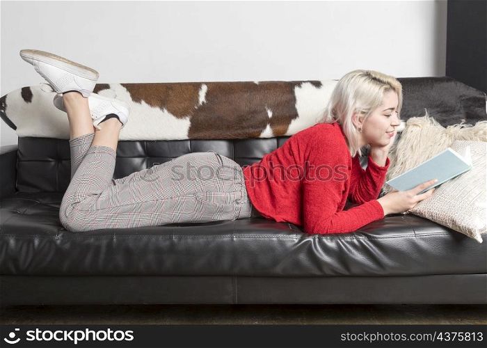Blonde woman reading a book on leather couch