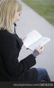 Blonde woman sits reading book outside on path