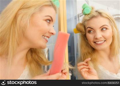 Blonde woman using hair rollers to create beautiful hairstyle on her hairdo.. Blonde woman using hair rollers