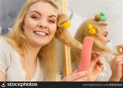 Blonde woman using hair rollers to create beautiful hairstyle on her hairdo.. Blonde woman using hair rollers