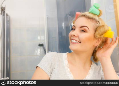 Blonde woman using hair rollers to create beautiful hairstyle on her hairdo.. Blonde woman using hair rollers