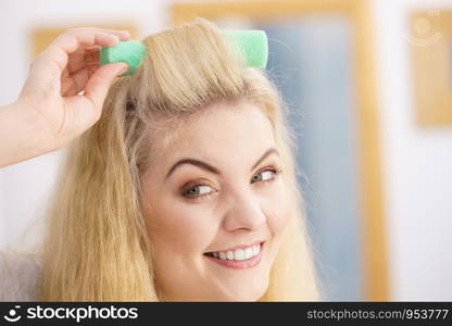 Blonde woman using hair rollers to create beautiful hairstyle on her hairdo.. Blonde woman using hair rollers