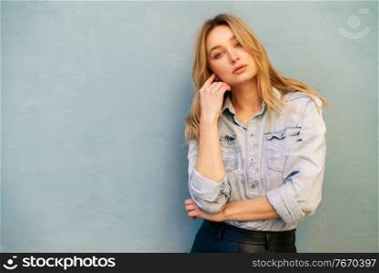 Blonde woman wearing denim shirt and black leather skirt standing in the street. Pretty russian female.. Blonde woman wearing denim shirt and black leather skirt standing in the street.