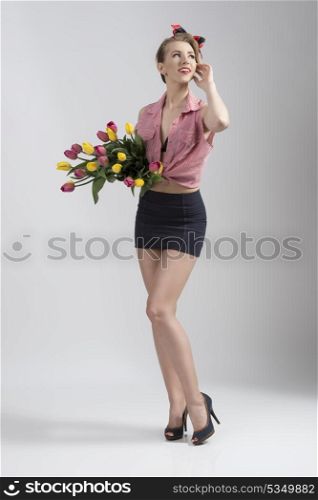 blonde woman wearing like pin-up with short skirt and open shirt posing in full-length portrait and taking coloured flowers in the hands