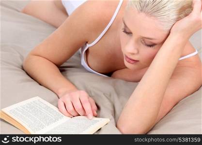 blonde woman with a decollete is reading a novel on a bed