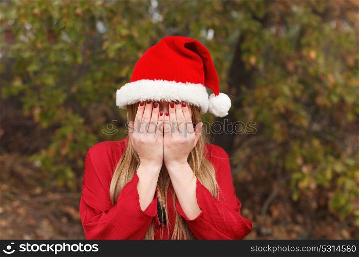 Blonde woman with Christmas hat covering her face in a park
