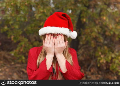 Blonde woman with Christmas hat covering her face in a park