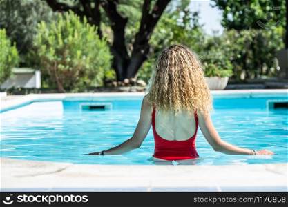 blonde woman with red swimsuit on her back in a swimming pool. summer concept