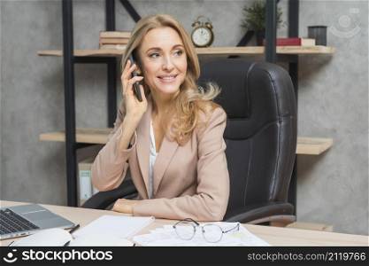 blonde young businesswoman talking cell phone sitting chair office