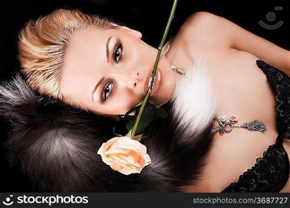 blonde young girl laying on black with a rose in her mouth