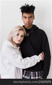 blonde young woman hugging her african boyfriend standing against white backdrop