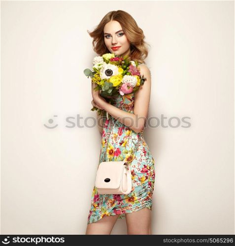 Blonde young woman in elegant floral dress. Girl posing on a beige background with handbag. Jewelry and hairstyle. Lady with spring bouquet of flowers. Fashion photo