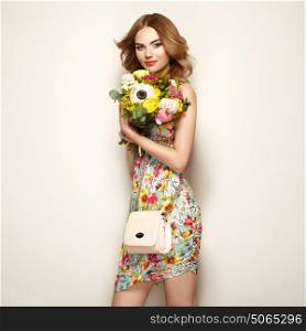 Blonde young woman in elegant floral dress. Girl posing on a beige background with handbag. Jewelry and hairstyle. Lady with spring bouquet of flowers. Fashion photo