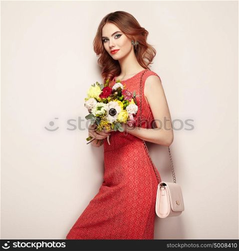 Blonde young woman in elegant red dress. Girl posing on a beige background with handbag. Jewelry and hairstyle. Lady with spring bouquet of flowers. Fashion photo