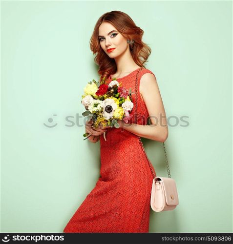 Blonde young woman in elegant red dress. Girl posing on a green background with handbag. Jewelry and hairstyle. Lady with spring bouquet of flowers. Fashion photo