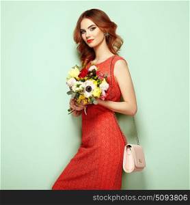 Blonde young woman in elegant red dress. Girl posing on a green background with handbag. Jewelry and hairstyle. Lady with spring bouquet of flowers. Fashion photo