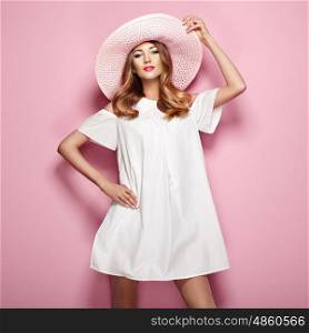 Blonde young woman in elegant white dress and summer hat. Girl posing on a pink background. Jewelry and clothing. Fashion photo