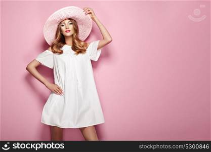 Blonde Young Woman in elegant white Dress and Summer Hat. Girl posing on a Pink Background. Jewelry and Clothing. Fashion photo