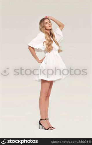 Blonde young woman in elegant white dress. Model posing on a white background in full length. Jewelry and hairstyle. Fashion photo