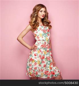 Blonde young woman in floral spring summer dress. Girl posing on a pink background. Summer floral outfit. Stylish wavy hairstyle. Fashion photo. Blonde lady