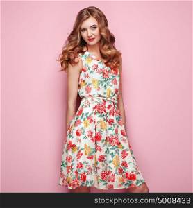 Blonde young woman in floral spring summer dress. Girl posing on a pink background. Summer floral outfit. Stylish wavy hairstyle. Fashion photo. Blonde lady