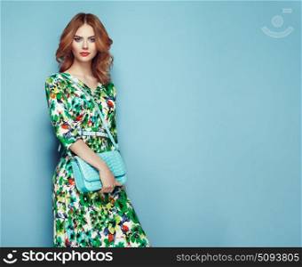 Blonde young woman in floral spring summer dress. Girl posing on a pink background. Summer floral outfit. Stylish wavy hairstyle. Fashion photo. Glamour lady with handbag