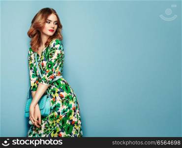Blonde young woman in floral spring summer dress. Girl posing on a pink background. Summer floral outfit. Stylish wavy hairstyle. Fashion photo. Glamour lady with handbag