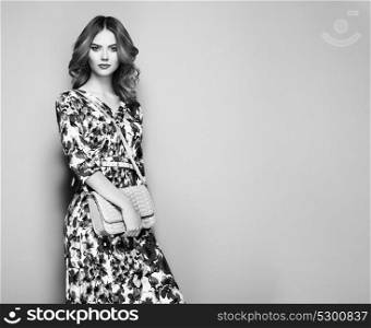 Blonde Young Woman in Floral Spring Summer Dress. Girl posing on a White Background. Stylish Wavy Hairstyle. Fashion photo. Glamour Lady with Handbag. Black and White photo