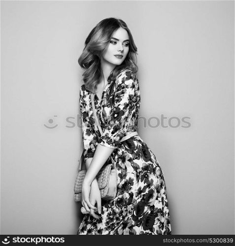 Blonde Young Woman in Floral Spring Summer Dress. Girl posing on a White Background. Stylish Wavy Hairstyle. Fashion photo. Glamour Lady with Handbag. Black and White photo