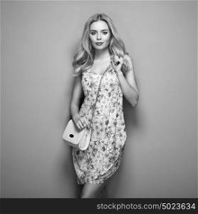 Blonde young woman in floral summer dress. Girl posing on a green background. Jewelry and hairstyle. Girl with handbag. Fashion photo. Black and White photo