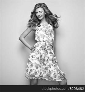 Blonde young woman in floral summer dress. Girl posing on white background. Stylish wavy hairstyle. Fashion Black and White photo. Blonde lady