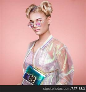 Blonde Young Woman in Holographic Jacket. Lady in Stylish Pink Eyeglasses. Model with Holographic Foil Handbags. Beauty Fashion Make-up