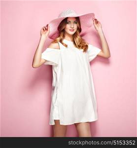 Blonde young woman in summer white dress and summer hat. Girl posing on a pink background. Jewelry and clothing. Fashion photo