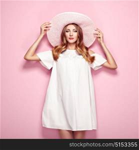 Blonde young woman in summer white dress and summer hat. Girl posing on a pink background. Jewelry and clothing. Fashion photo