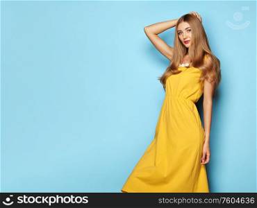 Blonde Young Woman in Yellow Spring Summer Dress. Lady in Stylish Summer Outfit. Girl Posing on a Blue Background. Stylish Hairstyle. Spring collection casual clothes