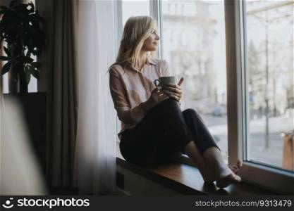 Blonde young woman relaxing and  drinking coffee by window
