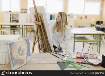 blonde young woman sitting workshop painting easel