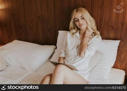 Blonde young woman using digital tablet on bed in the room